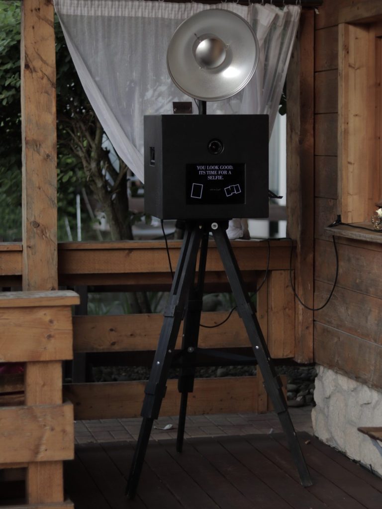 Fotobox schwarz Eine schwarze Fotobox mit einem großen Blitzlicht auf einem Stativ, umgeben von Dekoration.